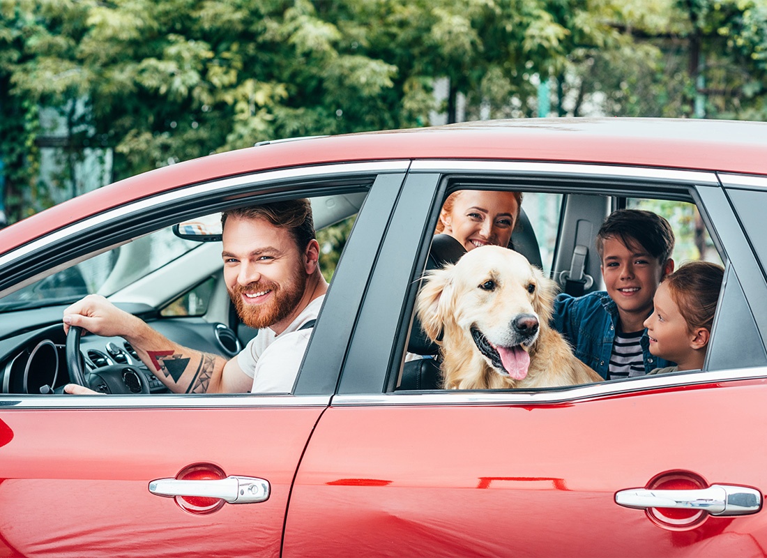 Personal Insurance - A Happy Family With Their Dog Riding in a Red Car While Smiling